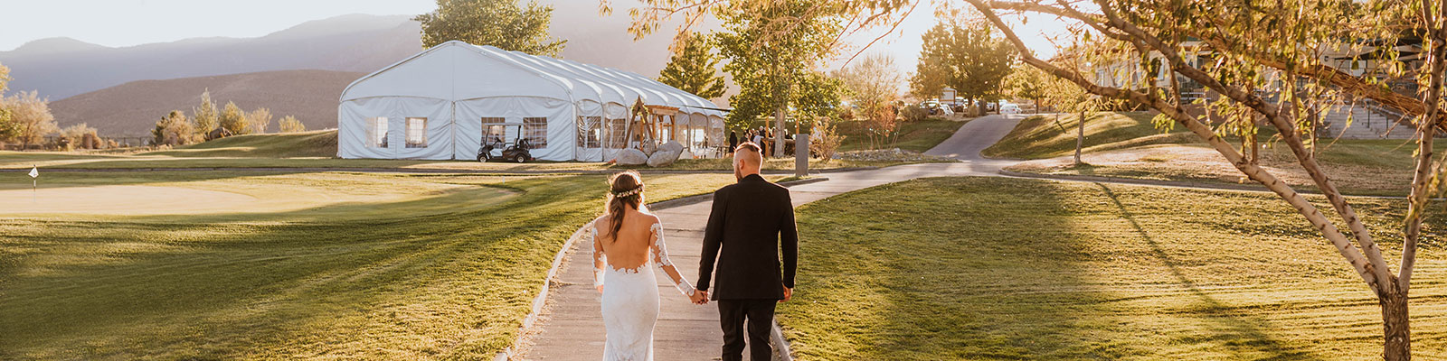 wedding couple holding hands and walking towards events tent at Sunridge Golf Course